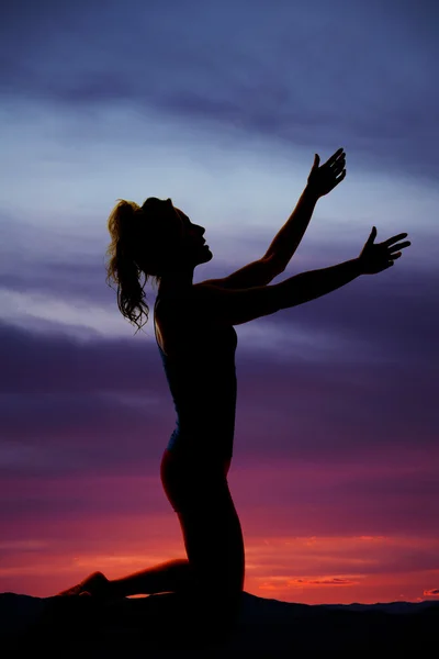 Silhouette of woman on her knees in the sunset reaching up with