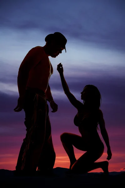 Silhouette of woman in bikini low reach up one hand to cowboy