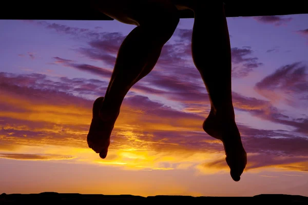 Silhouette of a womans legs hanging down in the colorful sunset