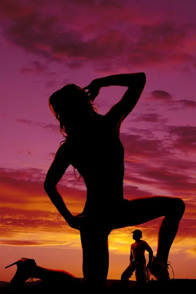 Silhouette of a woman on one knee and a cowboy in the background