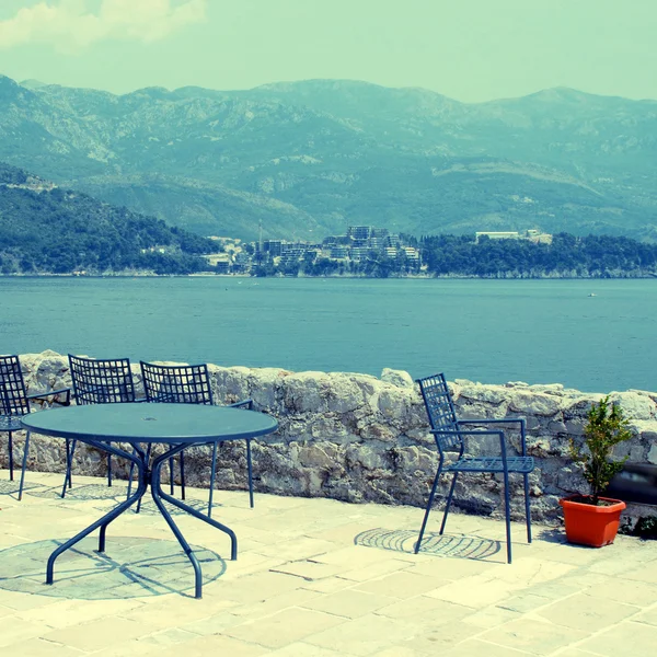 Blue iron chairs and table on stone terrace with sea view