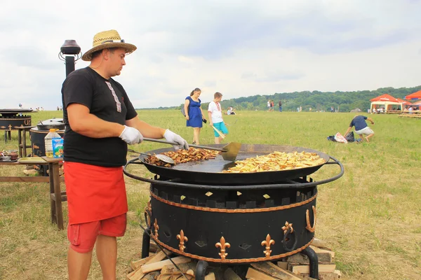 Man cooking crisp potato on the huge grill outdoor pan, Pirogovo, Kiev