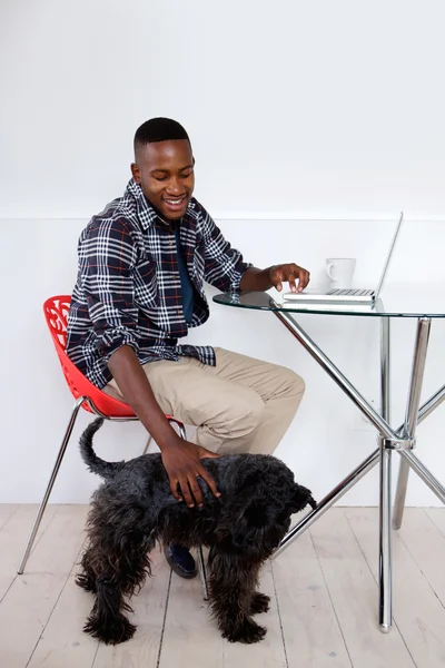 Young african man sitting at home with his pet dog and laptop
