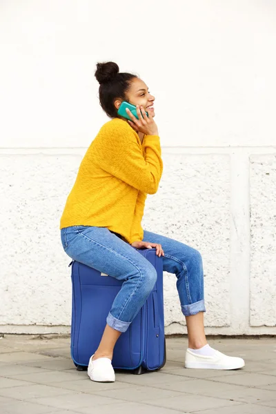 African woman sitting on suitcase and making phone call