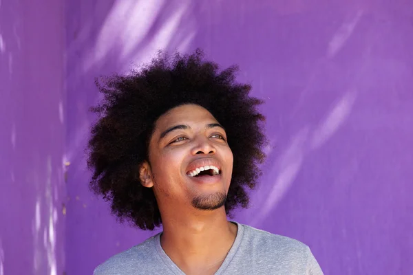 Carefree afro man laughing against purple wall