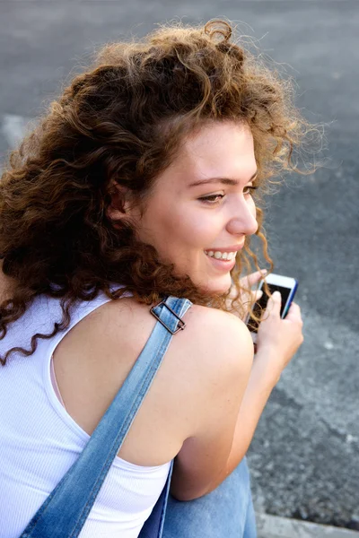 Smiling teen girl holding cellphone and sitting