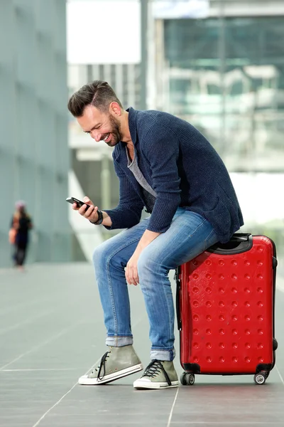 Middle aged man sitting on suitcase using mobile phone