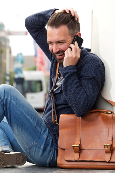 Cheerful guy sitting outdoors and talking on mobile phone