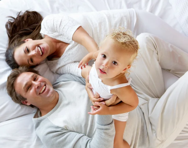 Family with cute little girl playing in bed