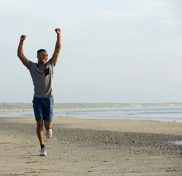 Young black man running on beach with arms raised