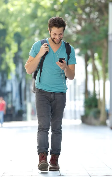 Smiling man walking in the city with mobile phone and bag