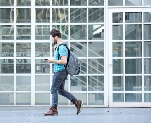 Male student walking on campus with bag and mobile phone