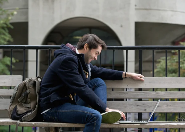 Young man sitting on bench smiling at laptop