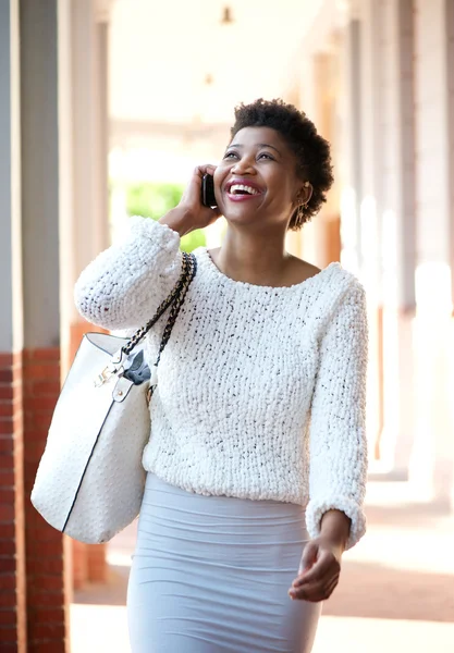 Smiling black woman walking and talking with cell phone