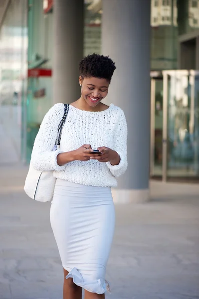 Smiling woman walking on sidewalk and sending text message