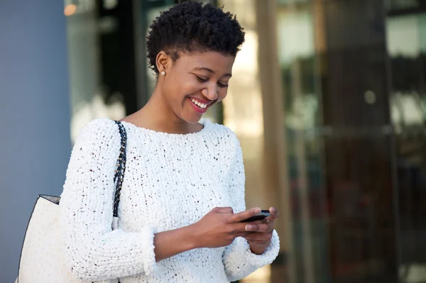 Happy young woman walking in the city sending text message