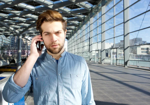 Serious young man talking on mobile phone inside building