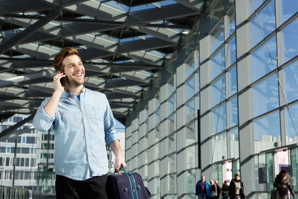 Young man smiling at station with bag and mobile phone