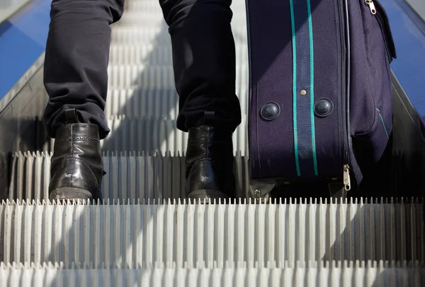 Man standing on escalator with travel bag