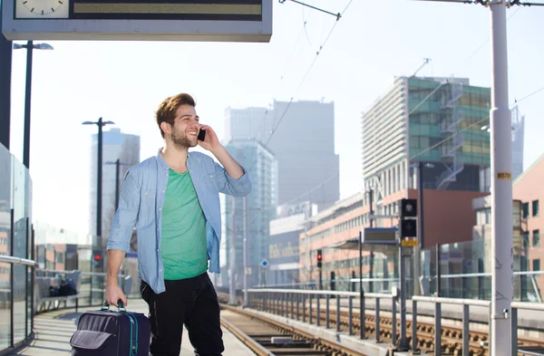 Happy young man talking on mobile phone at train station platform