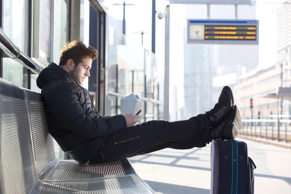 Man relaxing by train station platform with bag and mobile phone