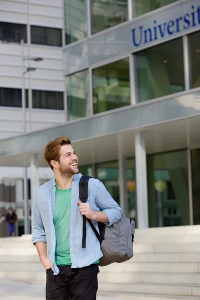 Happy male student standing on campus with bag