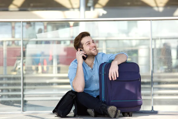 Man sitting with luggage and talking on mobile phone