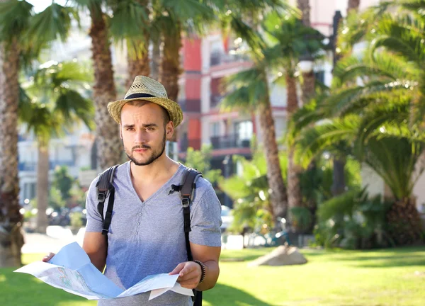 Young man standing alone outside with backpack and map