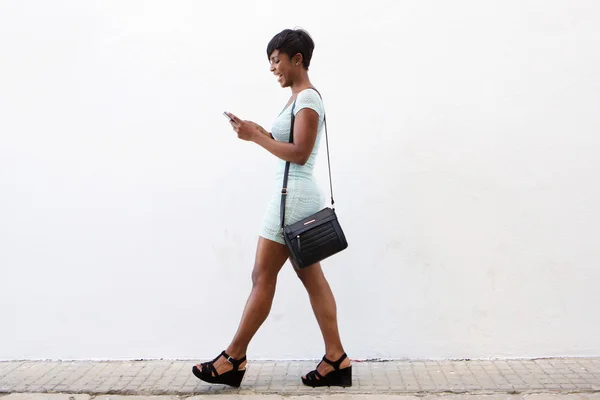 Smiling young woman walking and looking at cell phone