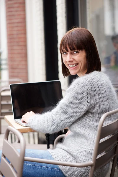 Middle aged woman sitting outside using laptop