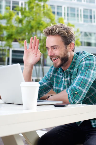 Smiling man waving hello on chat with laptop
