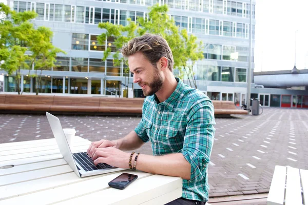 Attractive man smiling with laptop outside