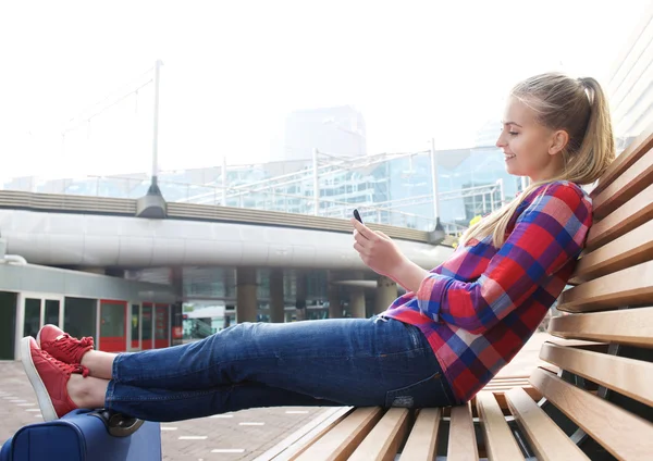 Smiling travel woman sitting outside looking at mobile phone