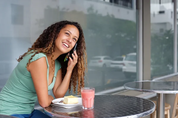 Smiling young woman sitting at a restaurant with mobile phone