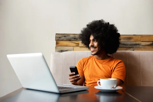 Smiling african american man sitting at table with mobile phone