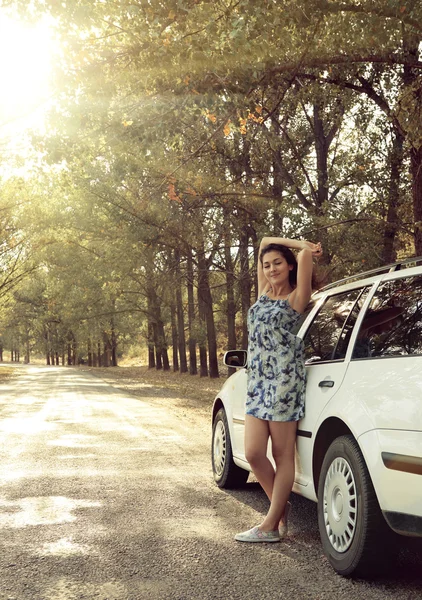 Girl stand near car on country road, bright sun and trees, summer season