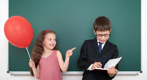 School boy and girl child with balloon on chalkboard background having fun