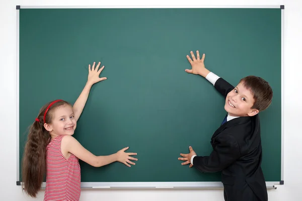 School boy and girl put hands on blank chalkboard and make frame, education concept