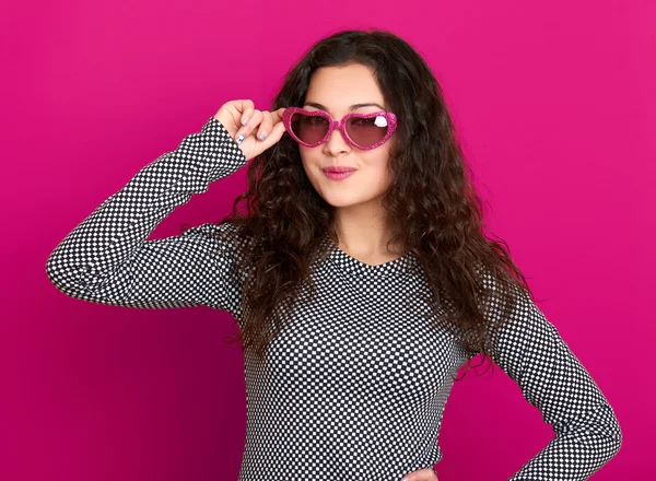 Young woman beautiful portrait, posing on pink background, long curly hair, sunglasses in heart shape, glamour concept