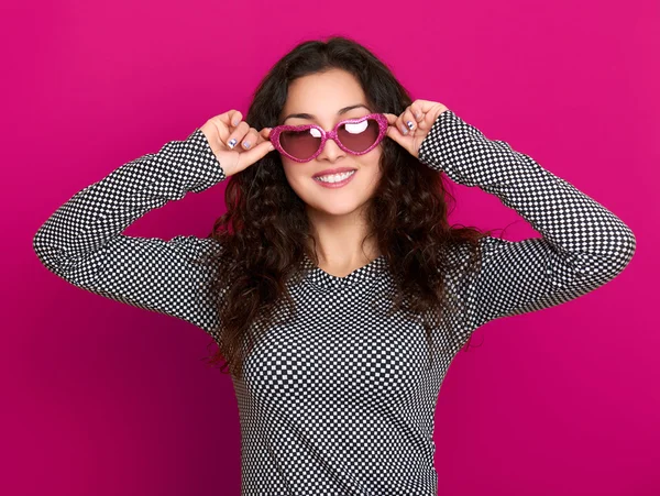 Young woman beautiful portrait, posing on pink background, long curly hair, sunglasses in heart shape, glamour concept