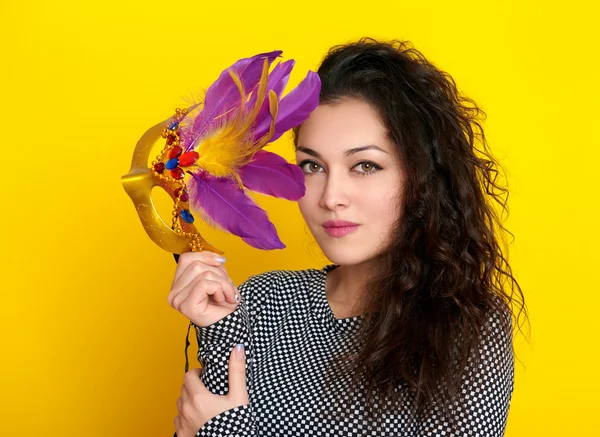 Woman in carnival mask with feather, beautiful girl portrait on yellow color background, long curly hair