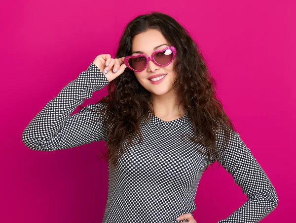 Young woman beautiful portrait, posing on pink background, long curly hair, sunglasses in heart shape, glamour concept
