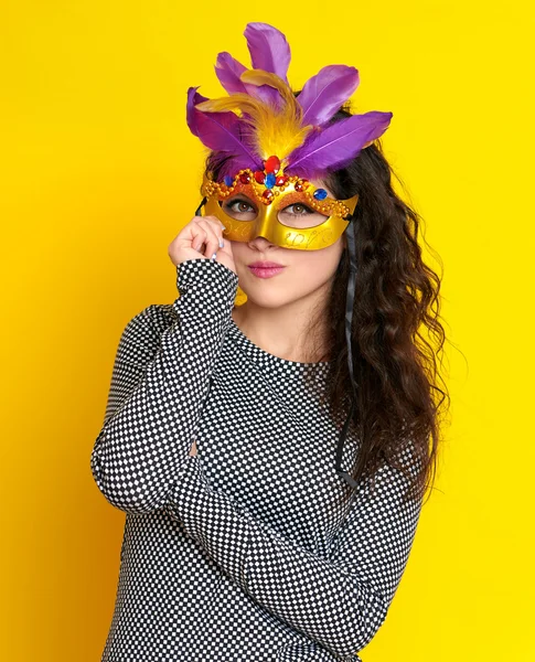 Woman in carnival masquerade mask with feather, beautiful girl portrait on yellow color background, long curly hair