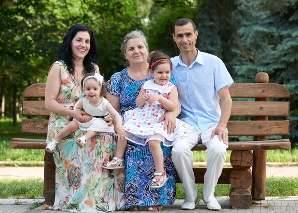 Big family sit on wooden bench in city park, summer season, child, parent and grandmother, small group of five people