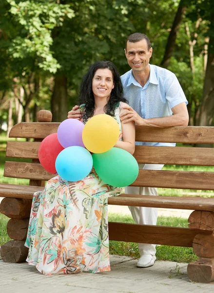 Happy romantic couple with balloon sit on bench in city park and posing, summer season, adult people man and woman