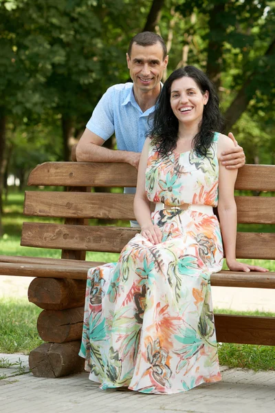 Romantic couple sit on bench in city park, summer season, adult happy people man and woman