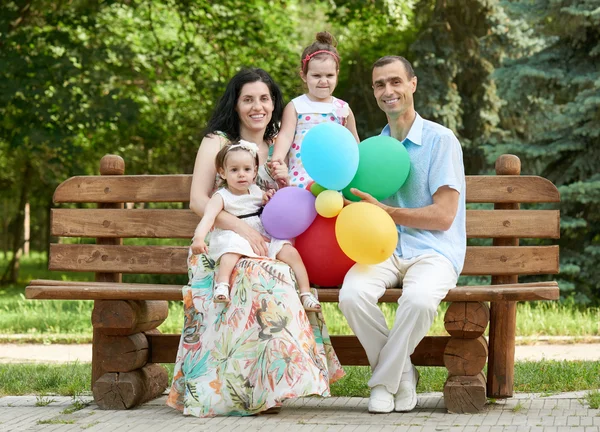 Happy family sit on wooden bench in city park, summer season, child and parent , group of four people