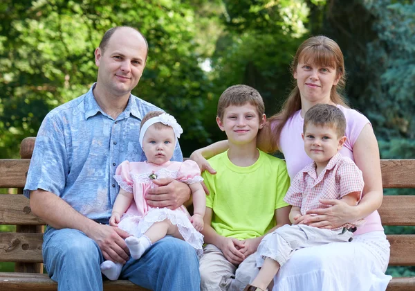 Happy family portrait on outdoor, group of five people sit on wooden bench in city park, summer season, child and parent