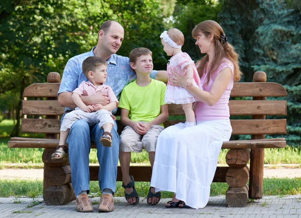 Happy family portrait on outdoor, group of five people sit on wooden bench in city park, summer season, child and parent