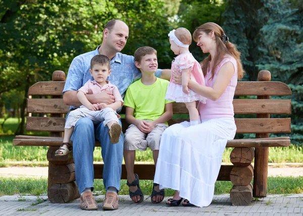 Happy family portrait on outdoor, group of five people sit on wooden bench in city park, summer season, child and parent